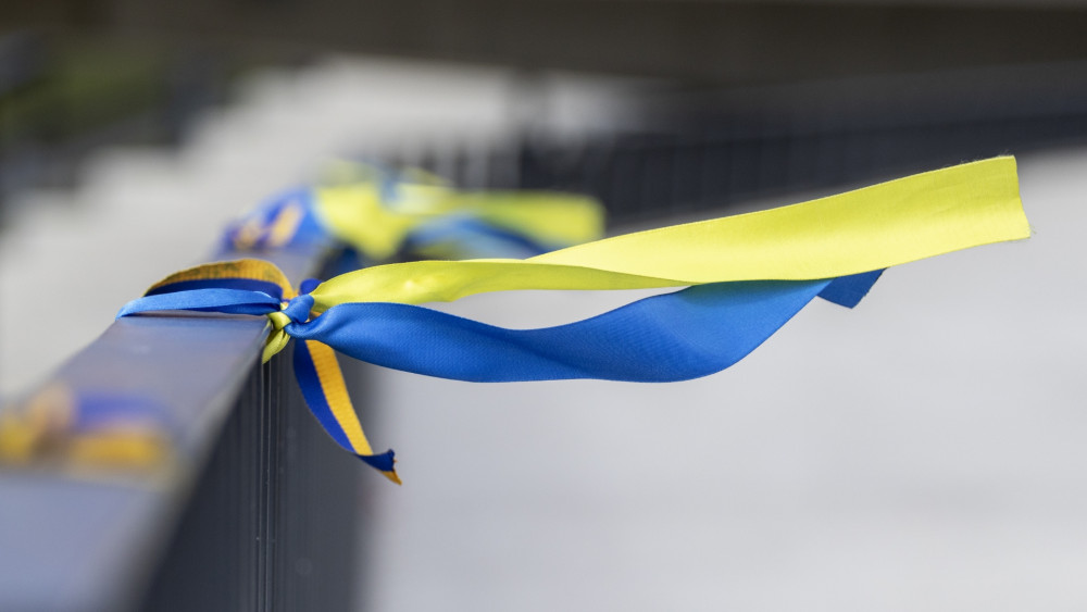 A ribbon with Ukrainian colors tied to a bridge, flying in the wind, representing international trade in the times of raw material shortage.